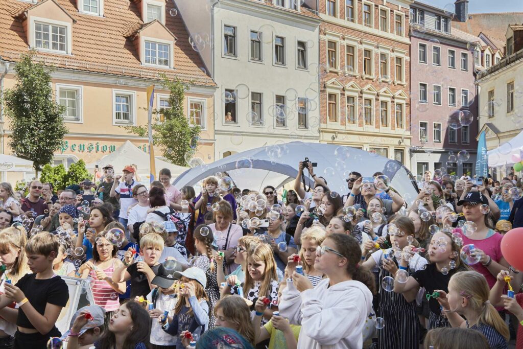 Zu sehen sind viele Kinder, die Seifenblasen in die Luft pusten.