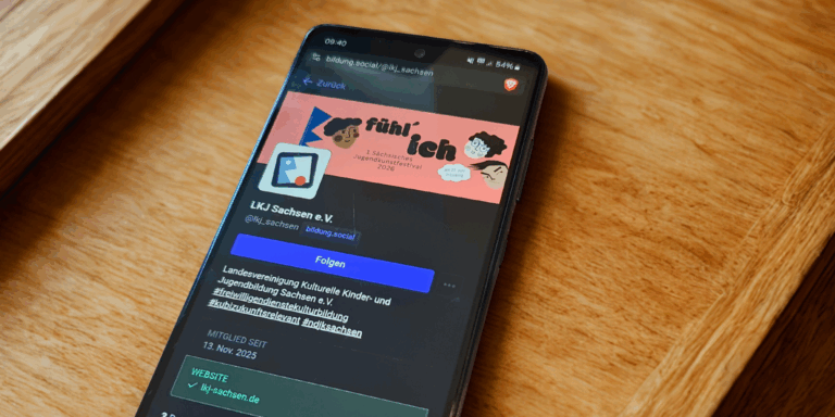 Bild: Ein Smartphone liegt auf einem Tisch. Auf dem Bildschirm ist die Mastodon-Seite der LKJ Sachsen zu sehen.