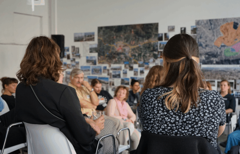 Rückansicht zweier Frauen mit dunklem Haar, die in einer Plenumssituation sitzen.