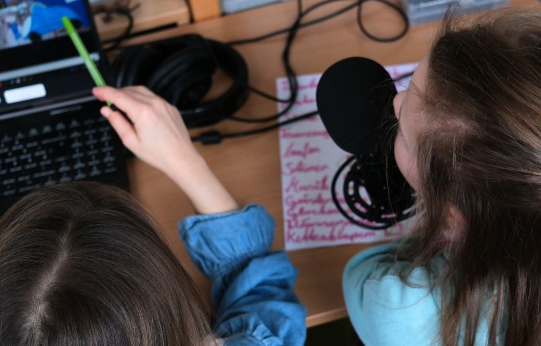 Zwei Kinder sitzen vor Bildschirmen. Ein Kind zeigt auf einen Monitor.